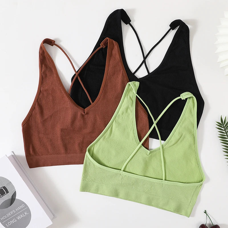Three seamless crop tops in brown, black, and green with stylish cross-back straps, perfect for women's streetwear.