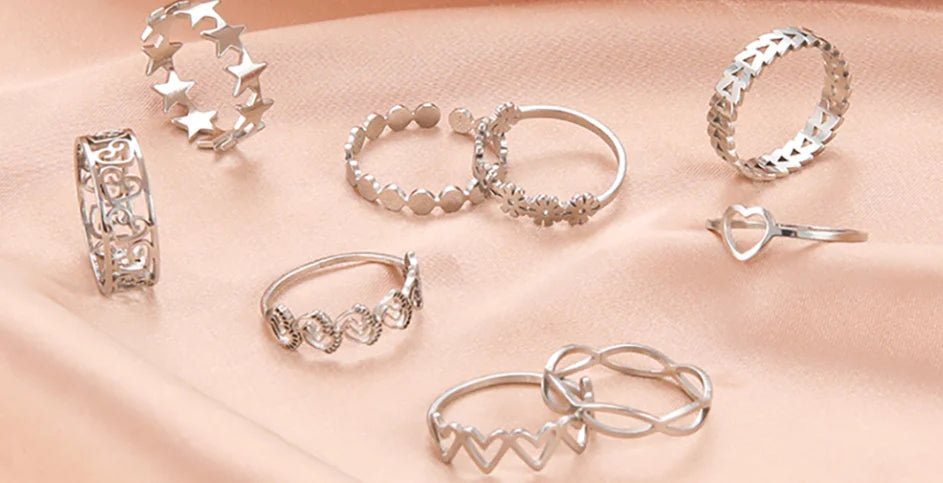 Assorted silver rings displayed on a soft pink fabric, featuring various designs for women.