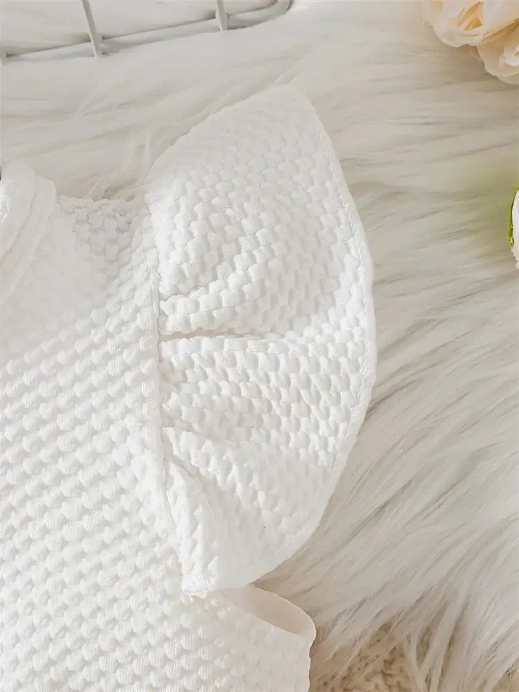 Close-up of a newborn girl’s dress featuring a textured white fabric with puffy short sleeves on a soft background.