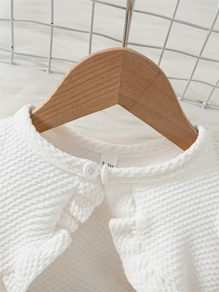 Close-up of a white newborn girl's dress on a wooden hanger, showcasing the fabric texture and button detail.