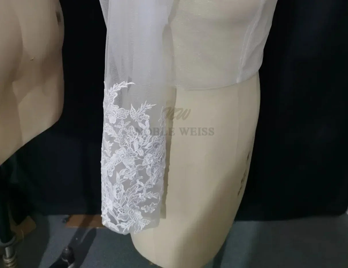 Lace bridal bolero with long sleeve and floral appliqué details, perfect as a wedding wrap by Noble Weiss.