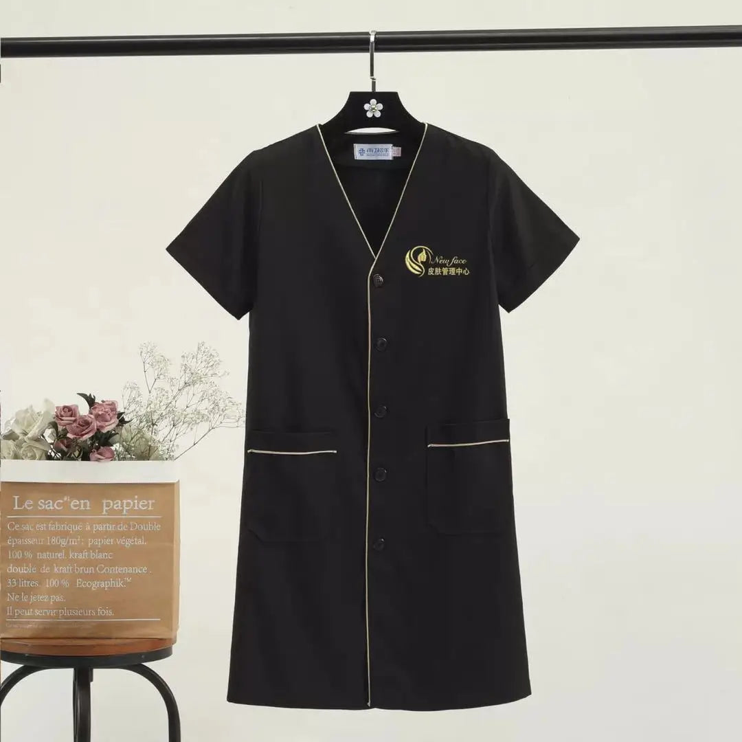 Custom black beauty uniform dress with pockets, short sleeves and logo for salons or spas.