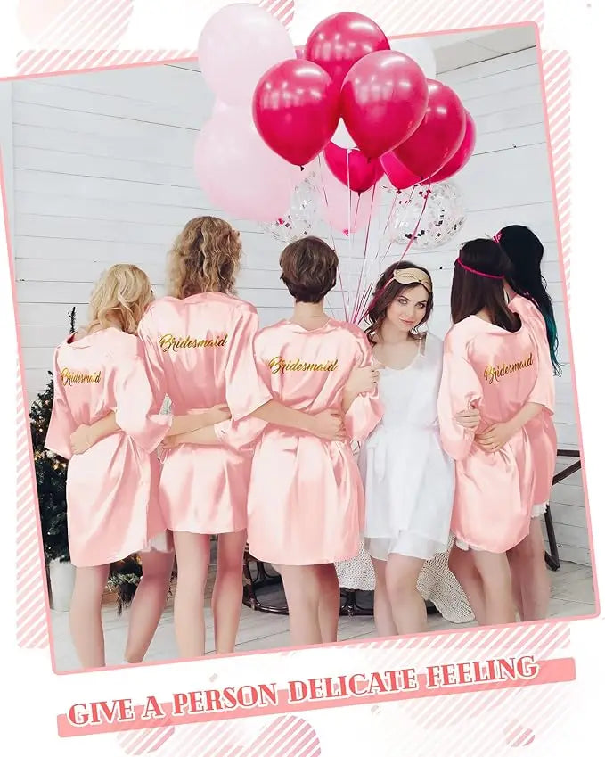 Group of bridesmaids in pink satin robes, celebrating a bridal shower with balloons.