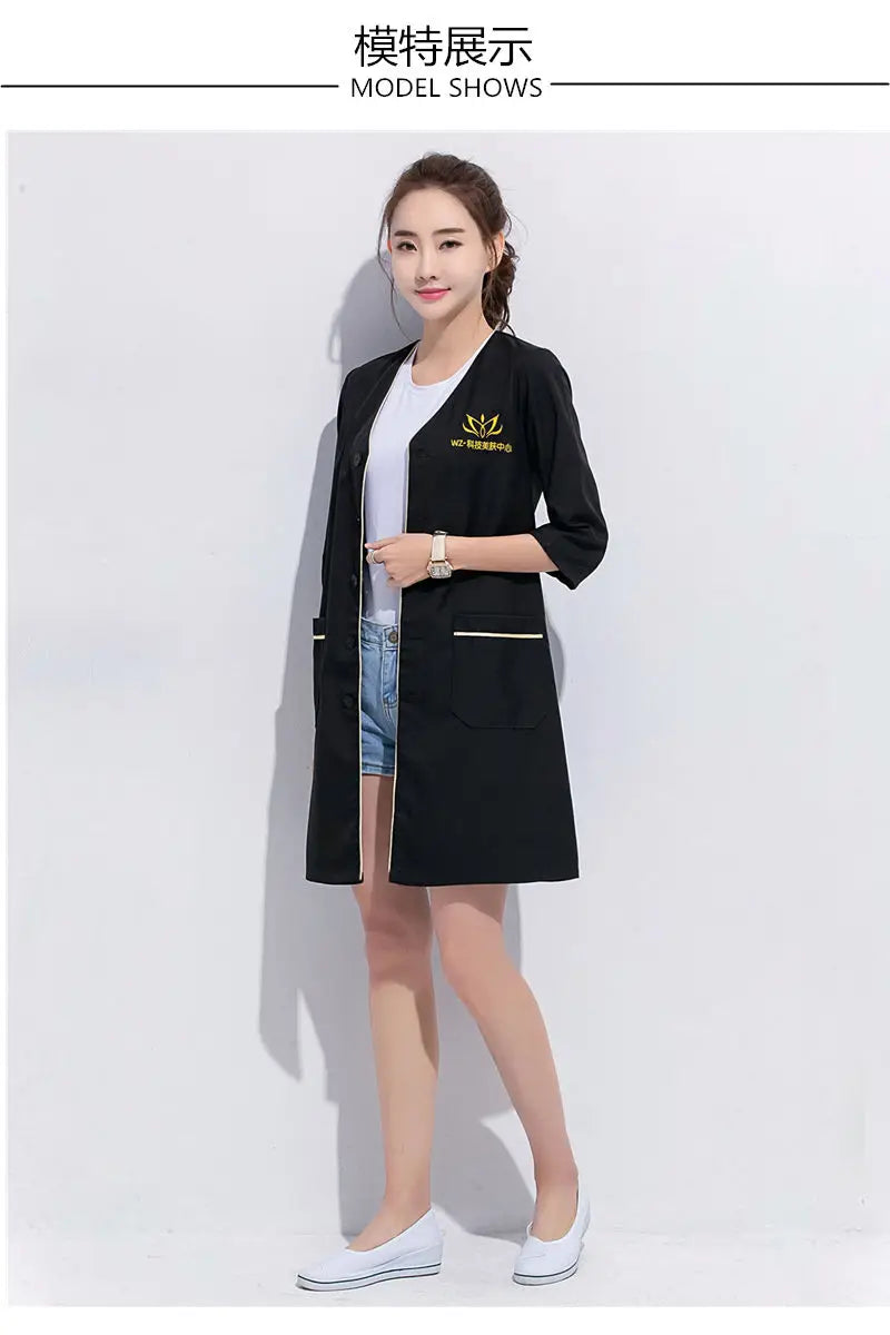 Model wearing a black salon beauty lab coat, showcasing pockets and stylish design, perfect for beauty professionals.