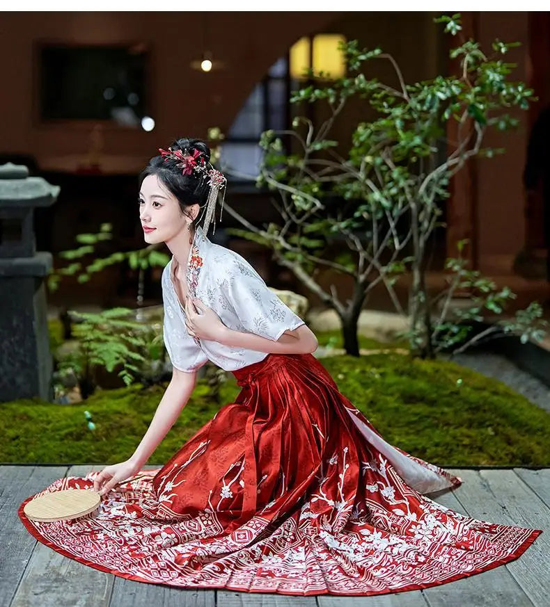 Woman wearing a traditional Hanfu oversized embroidered blouse with a red skirt, posed gracefully in a serene garden setting.