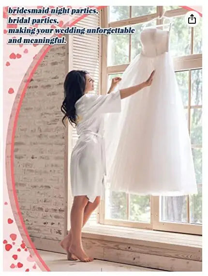 Woman in white robe admiring wedding dress by the window, perfect for bridal and bridesmaid celebrations.