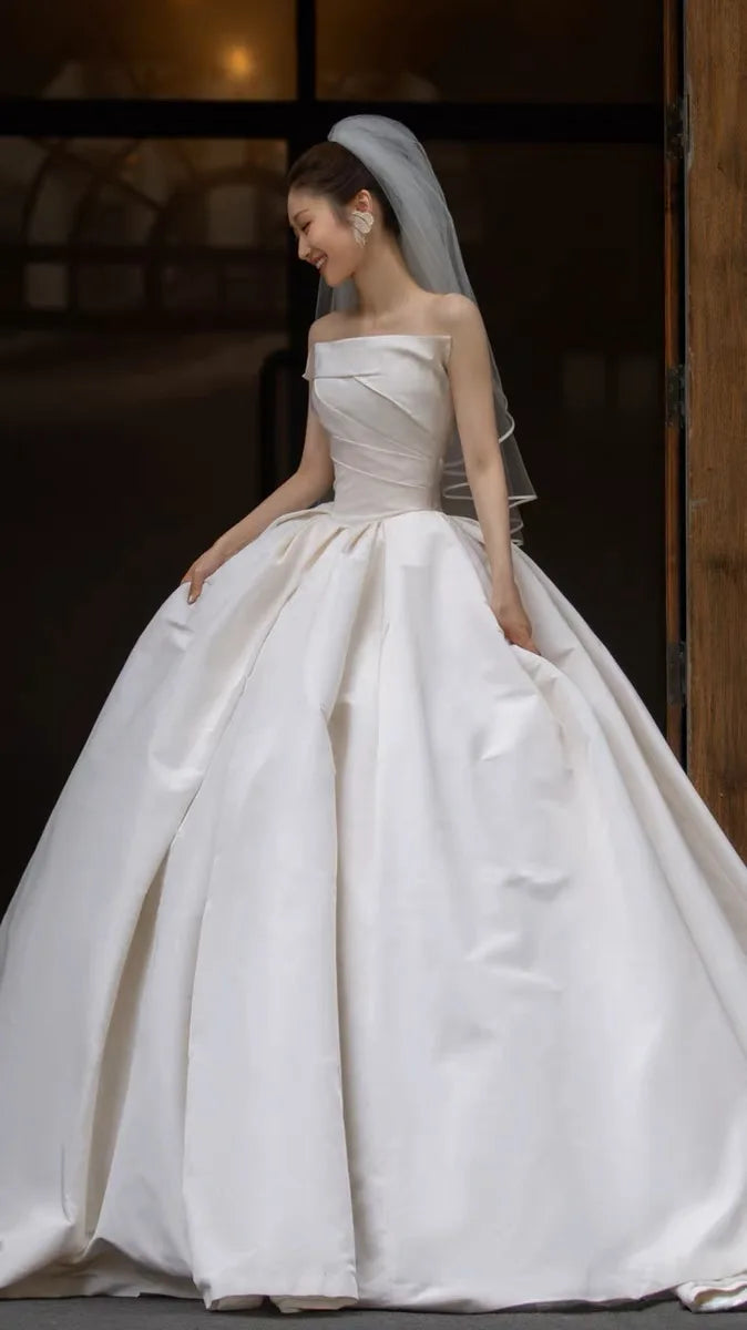 Bride in elegant satin wedding dress with off-shoulder design and full skirt, showcasing timeless bridal fashion.