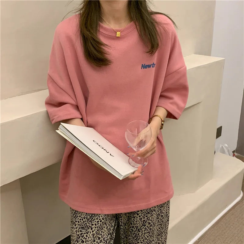 Oversized pink Harajuku streetwear tee on a woman holding a glass and a notebook, showcasing a trendy casual style.
