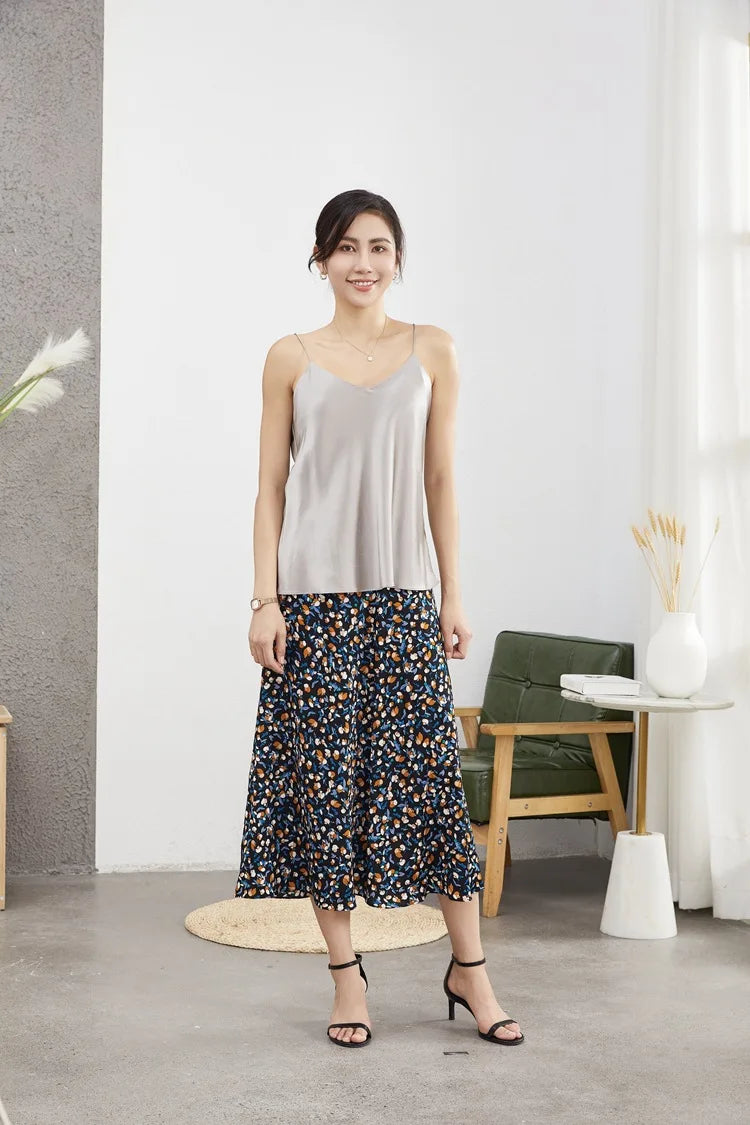 Woman wearing a stylish gray camisole and floral skirt in a modern interior, showcasing summer fashion.