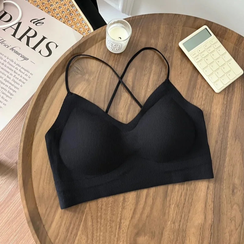 Black padded backless tank top on a wooden table, featuring stylish crisscross straps and ribbed fabric.