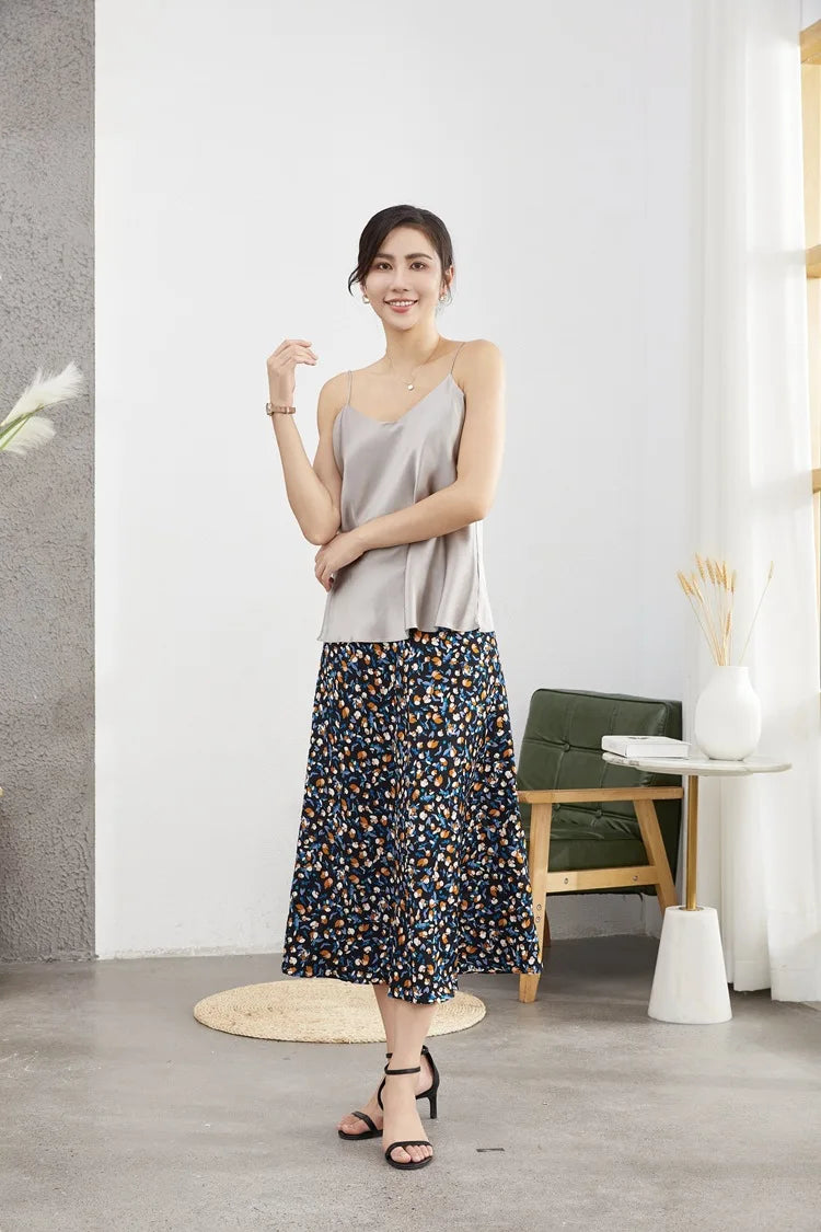 Model wearing a sleek silver satin camisole with a floral skirt, showcasing summer fashion style in a modern setting.