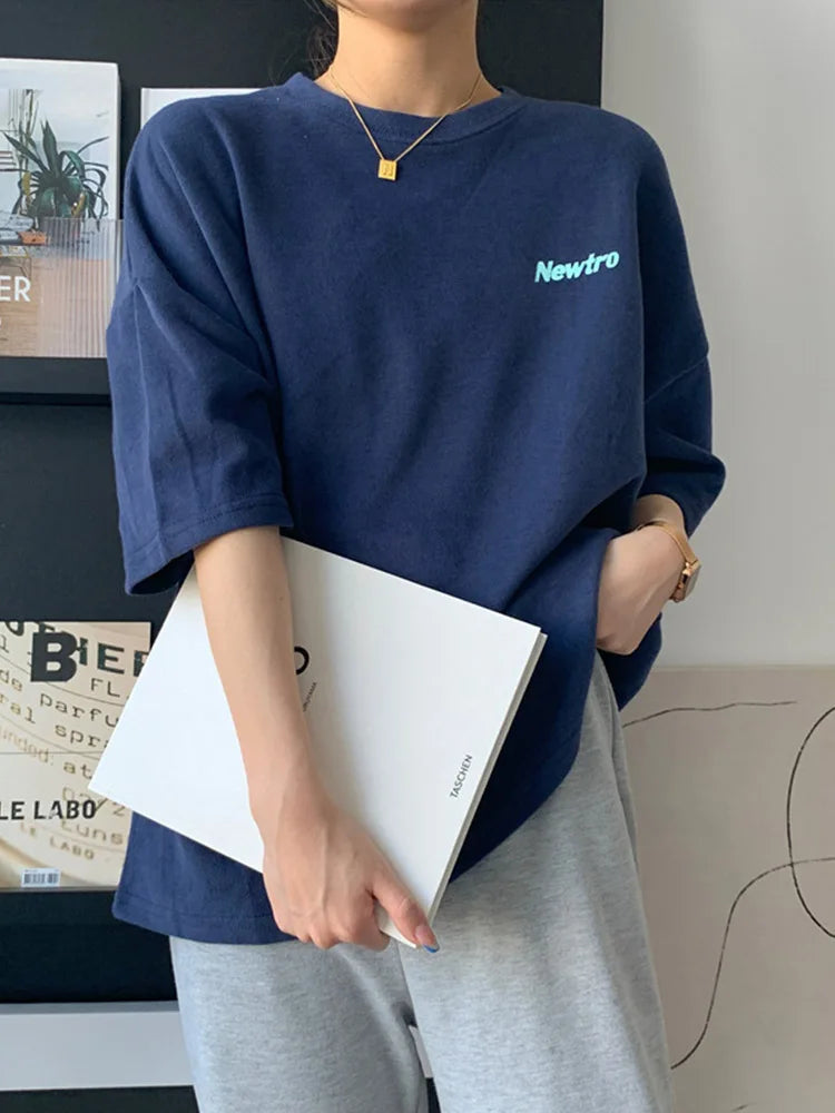 Oversized Harajuku streetwear tee in navy with 'Newtro' print, styled casually with gray pants and a notebook.