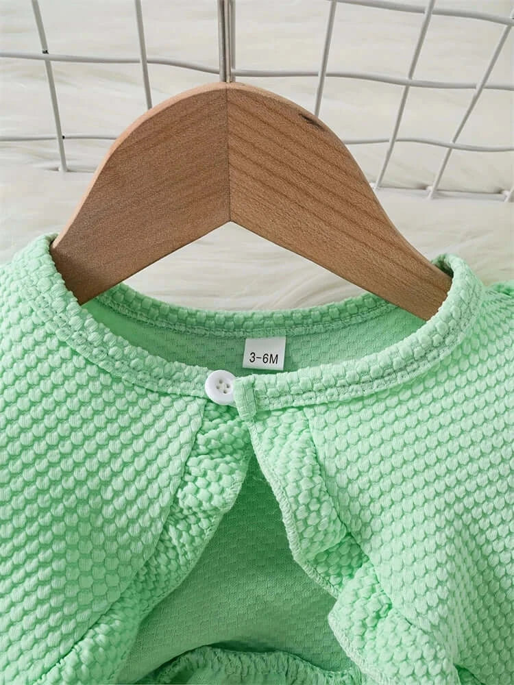 Close-up of a mint green baby dress with textured fabric and button closure hanging on a wooden hanger.