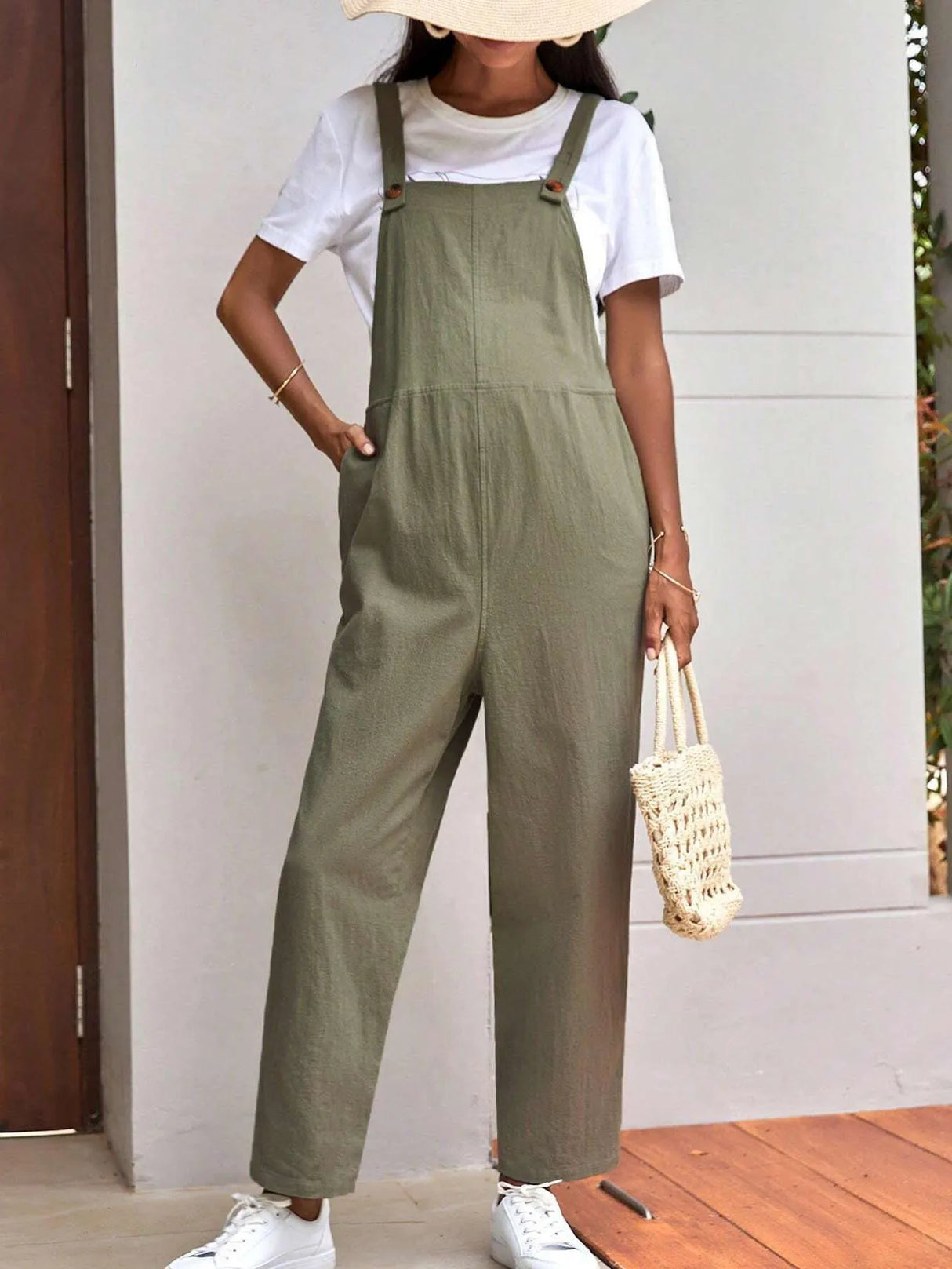 Stylish woman wearing adjustable maternity overalls in olive green, paired with a white tee and a woven bag.