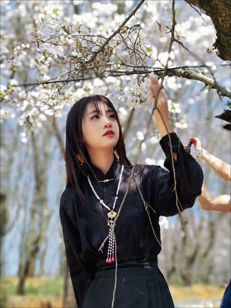 Woman wearing a traditional black Hanfu under cherry blossom trees, showcasing elegance and cultural heritage.