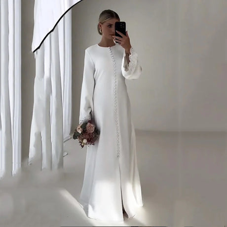 Elegant woman in a white satin gown with buttons, holding a bouquet, perfect for weddings or special occasions.