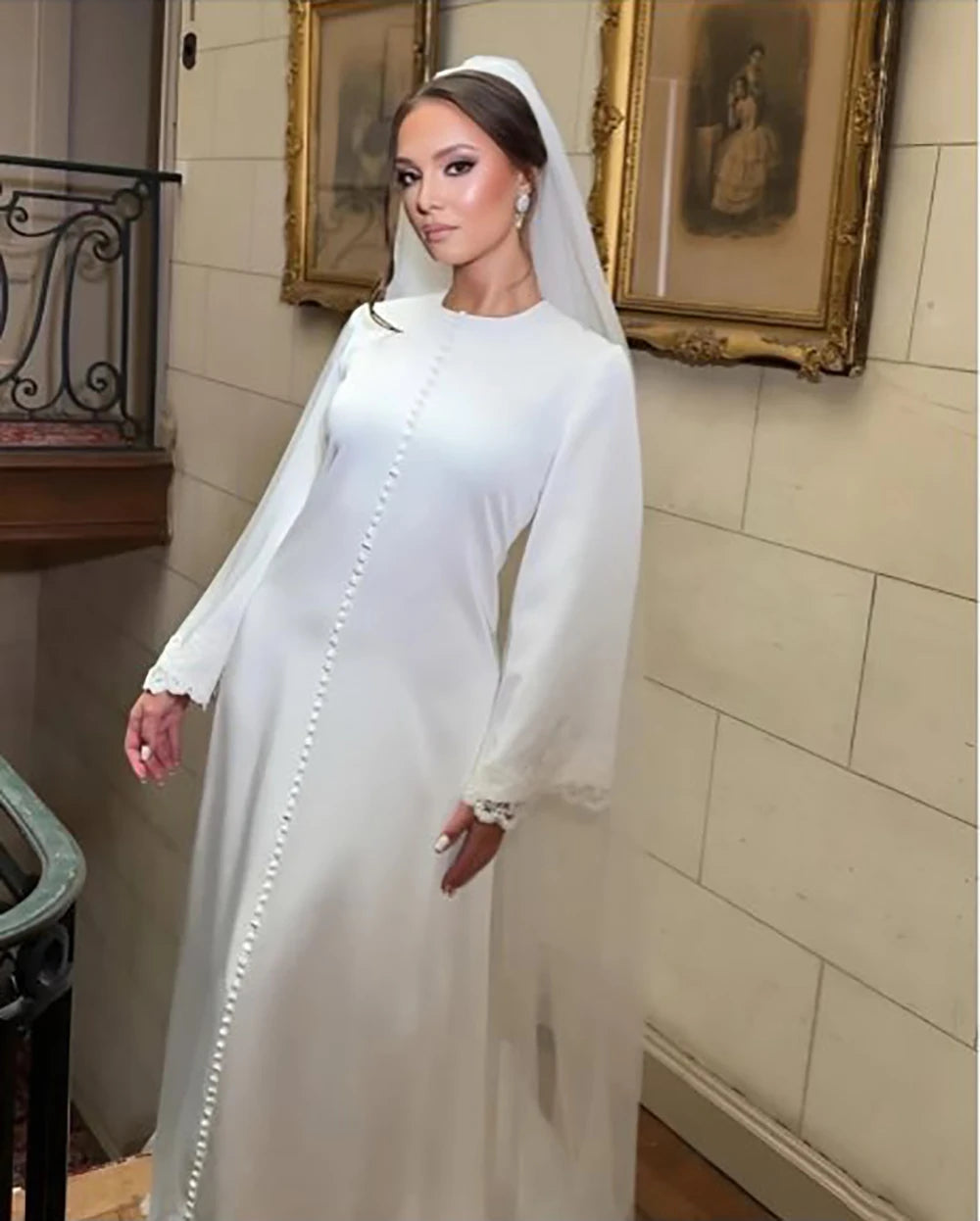 Elegant bride in a long-sleeve white wedding dress with button details and a veil, posing in a vintage setting.