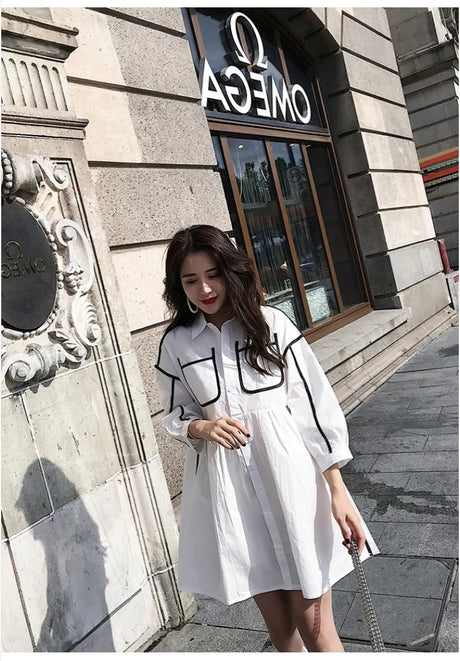 Model wearing a stylish white shirt dress with black detailing at a city street, perfect for casual outings.