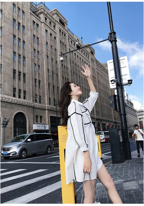 Woman in a solid color maternity shirt dress joyfully posing on a city street, showcasing summer style.