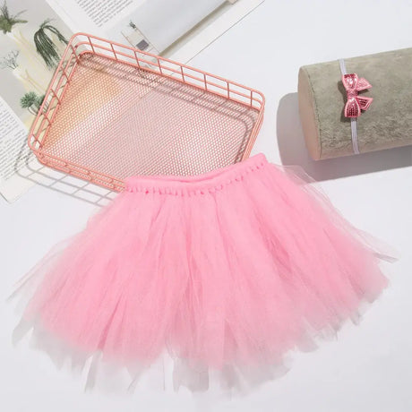 Pink infant tutu skirt on a white surface with a decorative tray and headband.