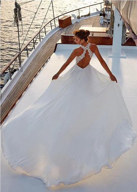 Bridal model in backless beach satin halter wedding dress with lace appliques, flowing on a yacht at sunset.