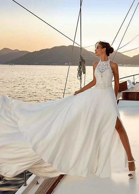 Elegant beach satin halter wedding dress with lace appliques and stylish slit, modeled by a bride at sunset.
