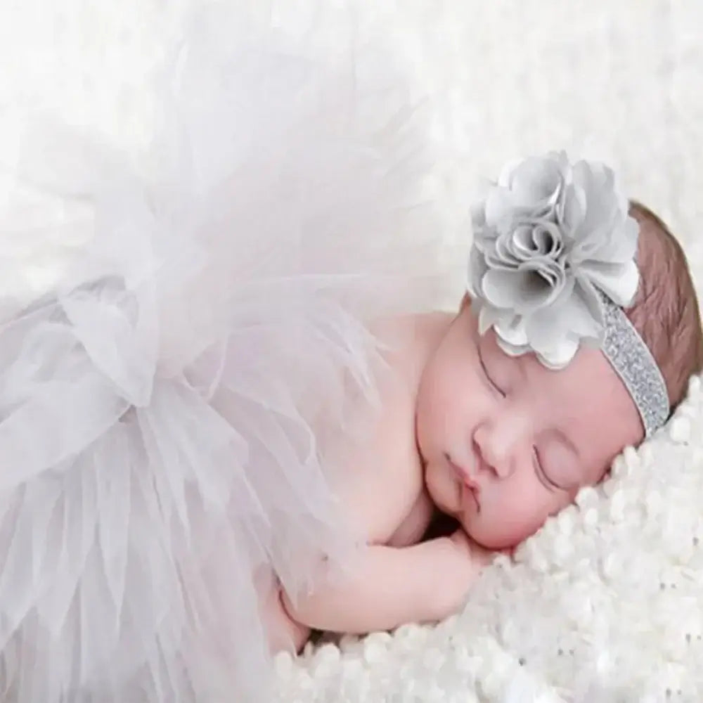 Newborn baby girl in a white tutu skirt and floral headband, perfect for photography sessions.