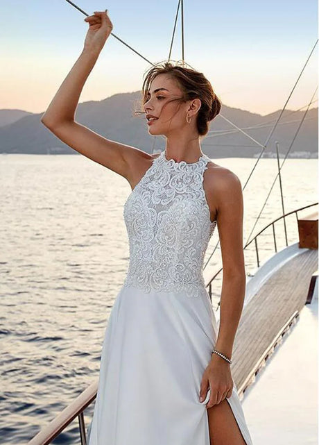 Model wearing a beach satin halter wedding dress with lace appliques and a slit, sailing on a boat at sunset.