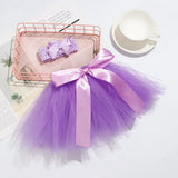 Infant purple tutu skirt with pink bow and matching headband on a white surface, ideal for baby photography.