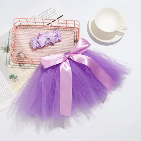 Infant purple tutu skirt with pink bow and matching headband on a white surface, ideal for baby photography.