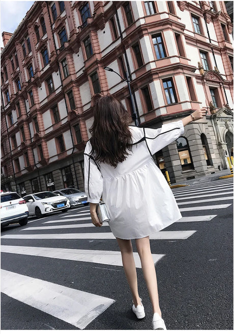 Woman wearing a solid color maternity shirt dress walking on a city street, showcasing summer style and comfort.