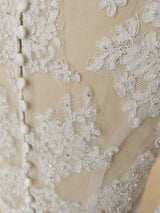 Close-up of crystal beaded wedding jacket fabric featuring intricate lace appliqué and button details.