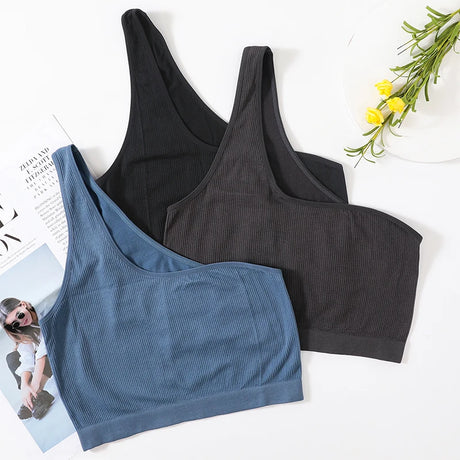 Three colors of MonoSculpt™ One-Shoulder Seamless Crop Tops displayed with a magazine and flowers.