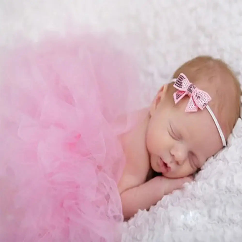 Newborn girl peacefully sleeping in a pink tutu and bow headband, ideal for photography accessories.