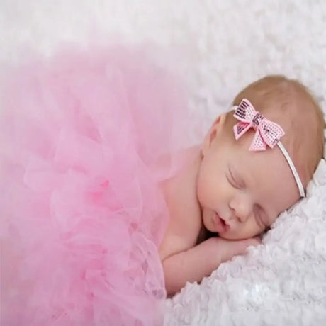 Newborn girl peacefully sleeping in a pink tutu and bow headband, ideal for photography accessories.