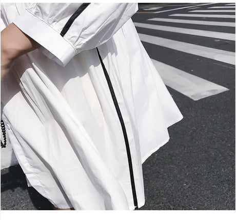 Close-up of a woman's white maternity shirt dress with black trim, perfect for summer beach outings.