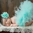 Newborn baby girl wearing a teal tutu skirt and floral headband, peacefully sleeping on a lace blanket.
