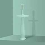 Soft silicone baby toothbrush displayed on a minimalist pedestal with a solid green background.