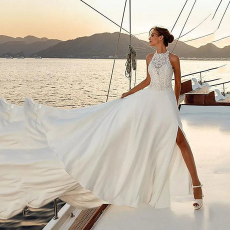 Beach satin halter wedding dress with lace appliques and slit, worn by a model on a boat at sunset.