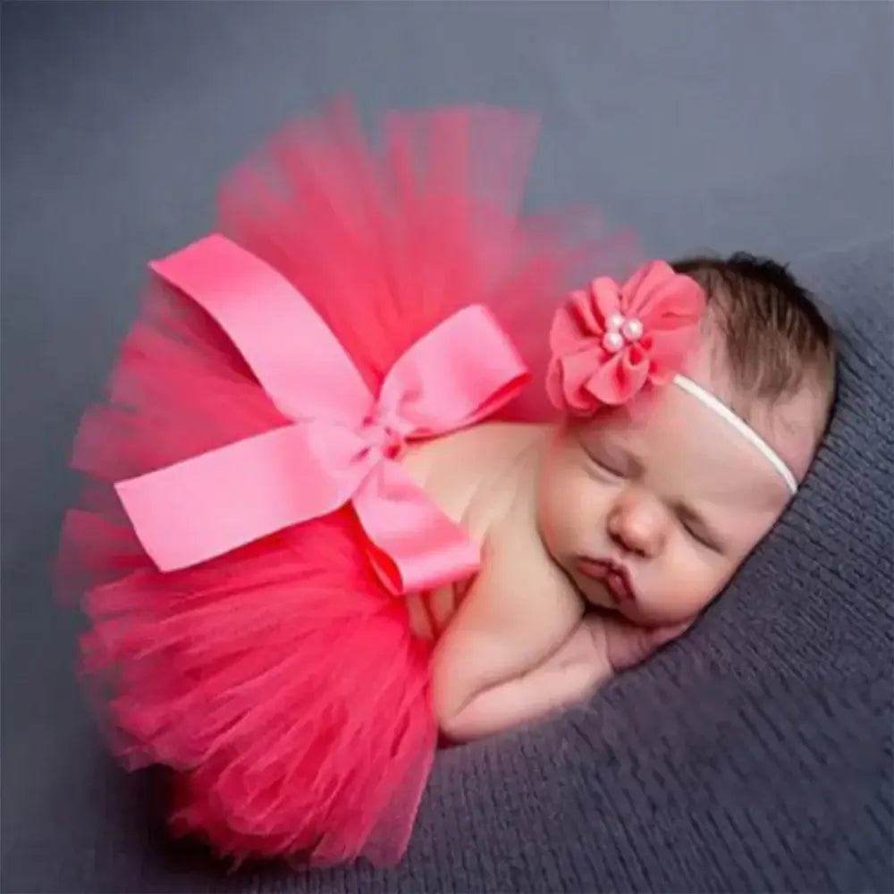 Infant girl sleeping in a pink tutu skirt with a matching flower headband, perfect for newborn photography.