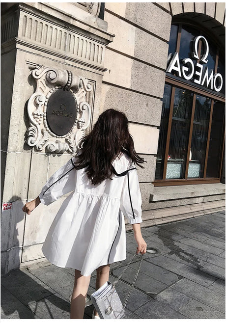 Back view of a woman wearing a white solid color maternity shirt dress with a turn-down collar.