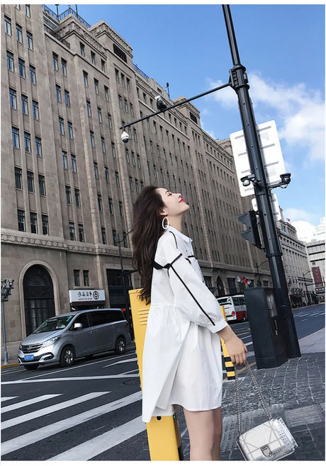 Woman in a stylish white shirt dress posing on the street, perfect for summer outings and beach parties.