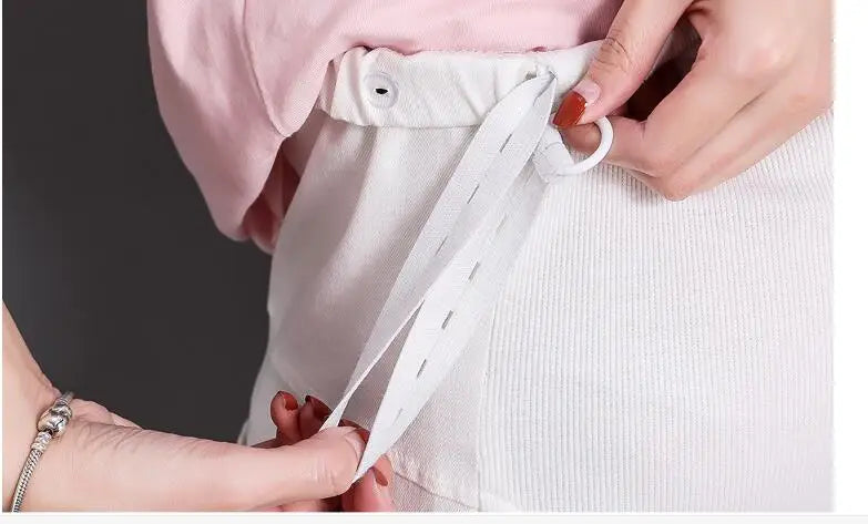 Close-up of hands adjusting the tie of casual 3-color maternity pants, showcasing the comfortable waistband design.