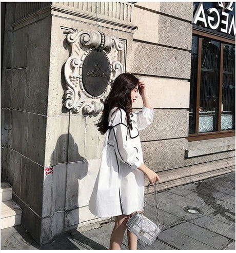 Woman wearing a solid color maternity shirt dress, posing outside a building with stylish architecture.