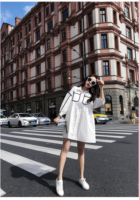 Woman wearing a solid color maternity shirt dress, posing stylishly on a city street.