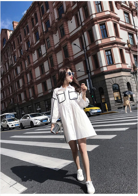 Model wearing a solid color maternity shirt dress with pockets, enjoying a summer day on a busy city street.