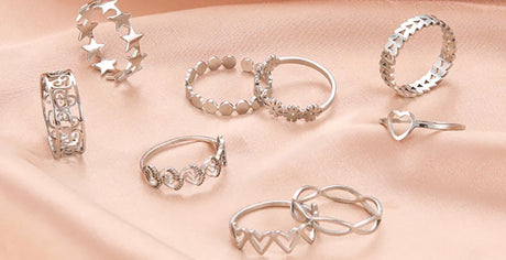 Assorted silver rings displayed on a soft pink fabric, featuring various designs for women.