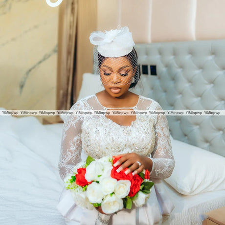 Bridal model wearing an African lace wedding dress with a crystal beaded design, holding a bouquet of red and white flowers.