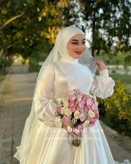 Muslim A-Line satin wedding dress with high collar, model holding bouquet, outdoor setting, elegant and modest look.