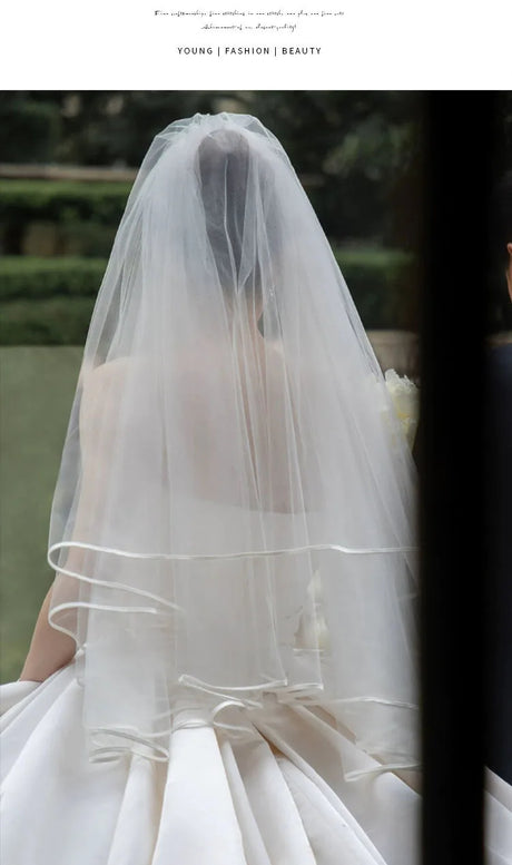 Elegant bride wearing a sheer veil and a satin wedding gown, showcasing simplicity and beauty.